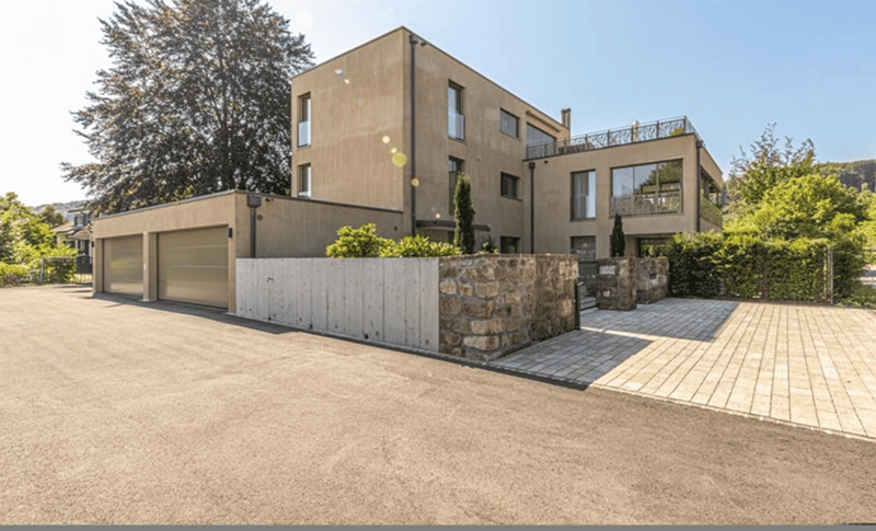Modern house, beige exterior, large windows, garage, driveway, stone wall, greenery