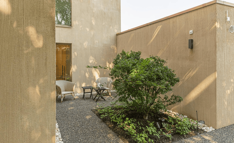 small garden with gravel, two chairs, small table, plant, beige walls