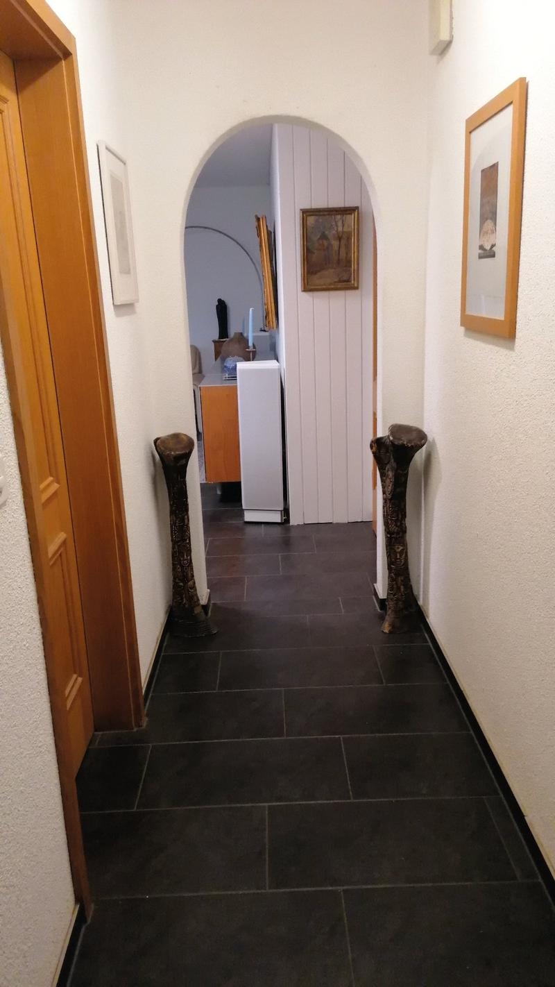 white walls, black tiles, wooden door, two wooden sculptures, two picture frames, arched doorway, white refrigerator, wooden cabinet, mirror