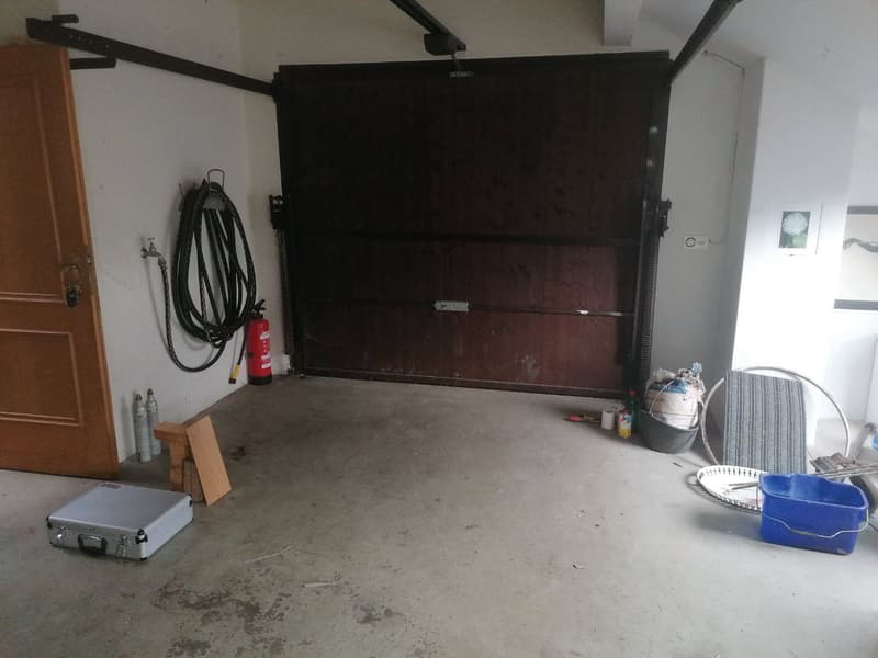 Garage with a wooden door, a fire extinguisher, a hose, and various items on the floor