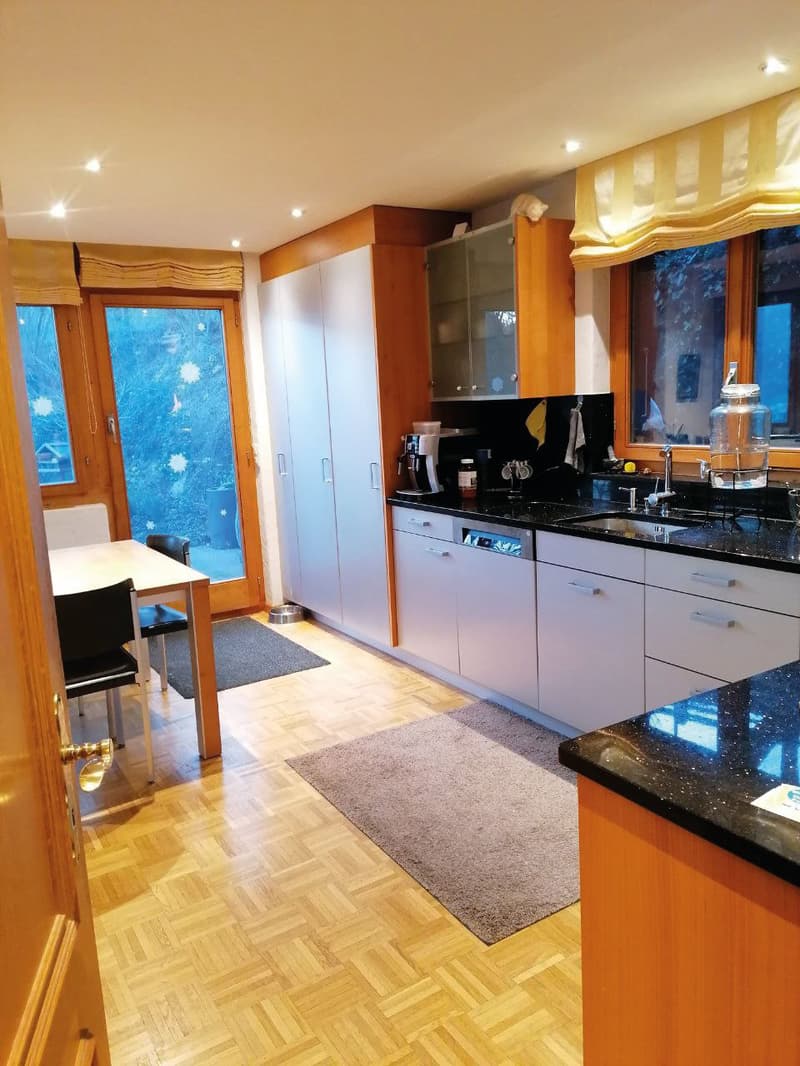 modern kitchen with wooden floor, white cabinets, black countertops, dishwasher, dining table, glass door
