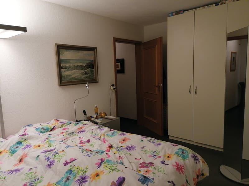 Bedroom with bed, nightstand, painting, wardrobe, and open door to another room