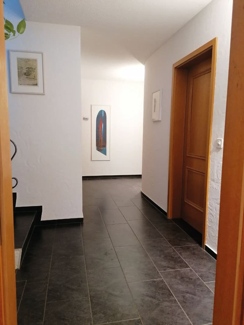 Empty hallway with white walls, black tiles, two framed pictures on the wall, wooden door.