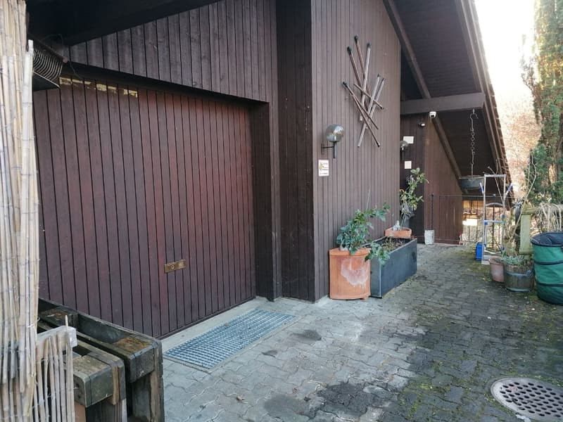 Exterior of a house with a wooden garage door, brick pathway, and potted plants.
