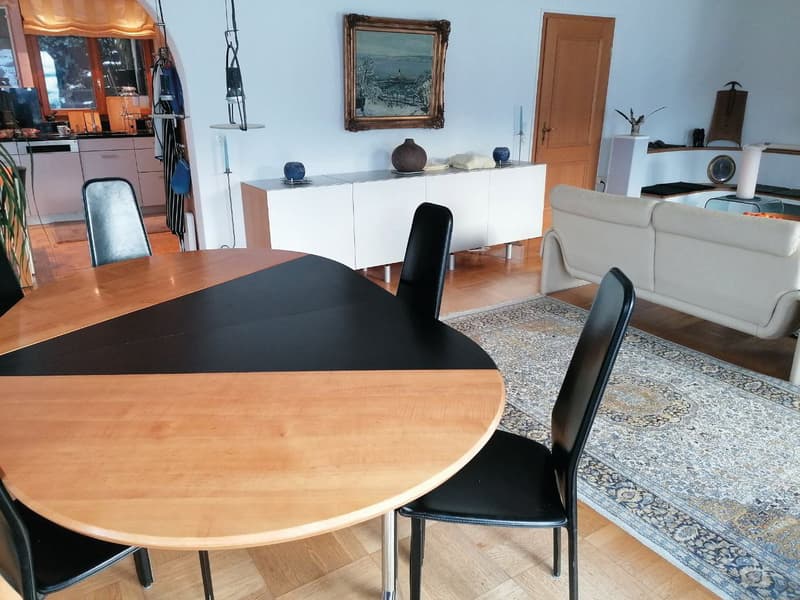 oval wooden table, black chairs, white sideboard, white couch, rug, picture frame, kitchen in background