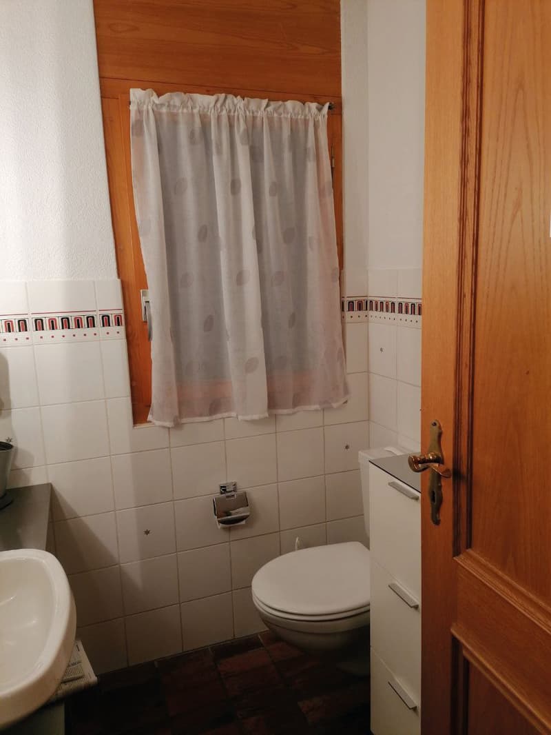 Bathroom with white tiles, white sink, white toilet, wooden window frame, white curtain, wooden door