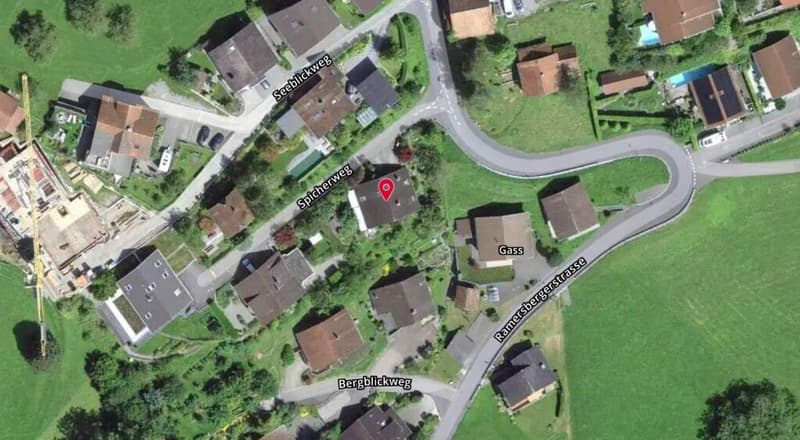 House located in a small village, surrounded by other houses and greenery, with a road leading to it.