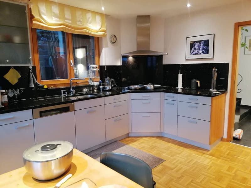 modern kitchen with black countertops, white cabinets, stainless steel appliances, wooden floor, large window, picture frame on wall