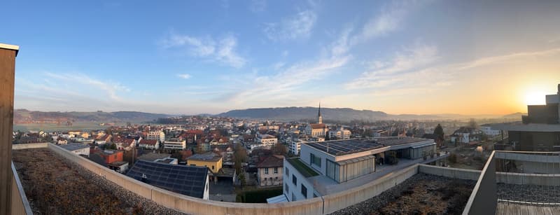 Aerial view of a city with many buildings, mountains in the distance, and a setting sun