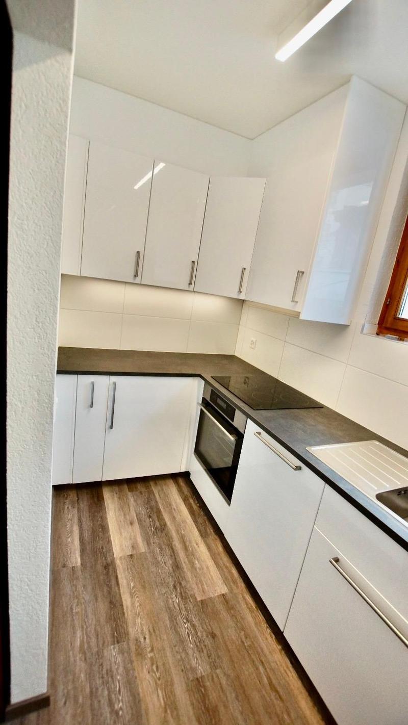 modern kitchen with white cabinets, wooden floor, black countertop, built-in oven, dishwasher, sink