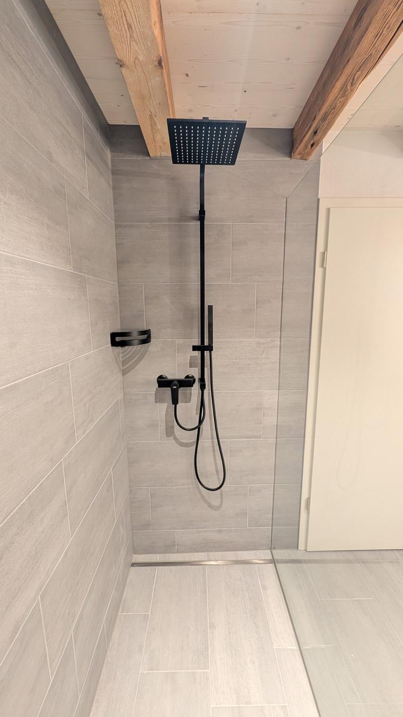 shower area with tiled walls, glass door, black shower head, wooden ceiling beams