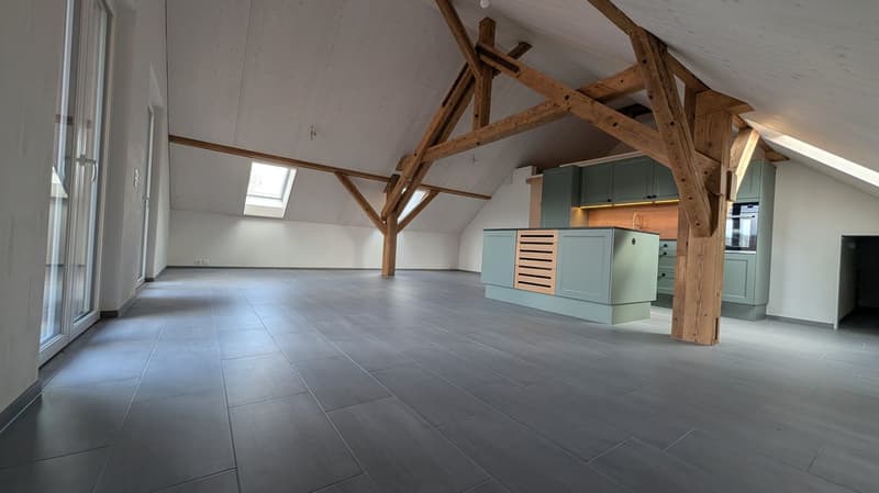 empty room, wooden beams, gray floor, kitchen area with cabinets and appliances