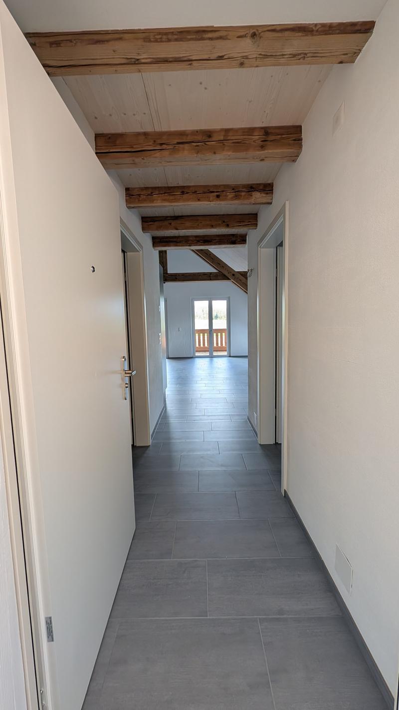 Empty corridor with wooden beams, tiled floor, and white walls.