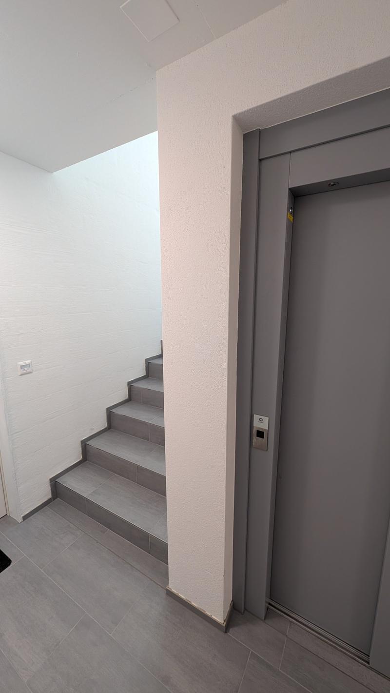 A corridor with tiled flooring, a staircase, and an elevator door with a button.