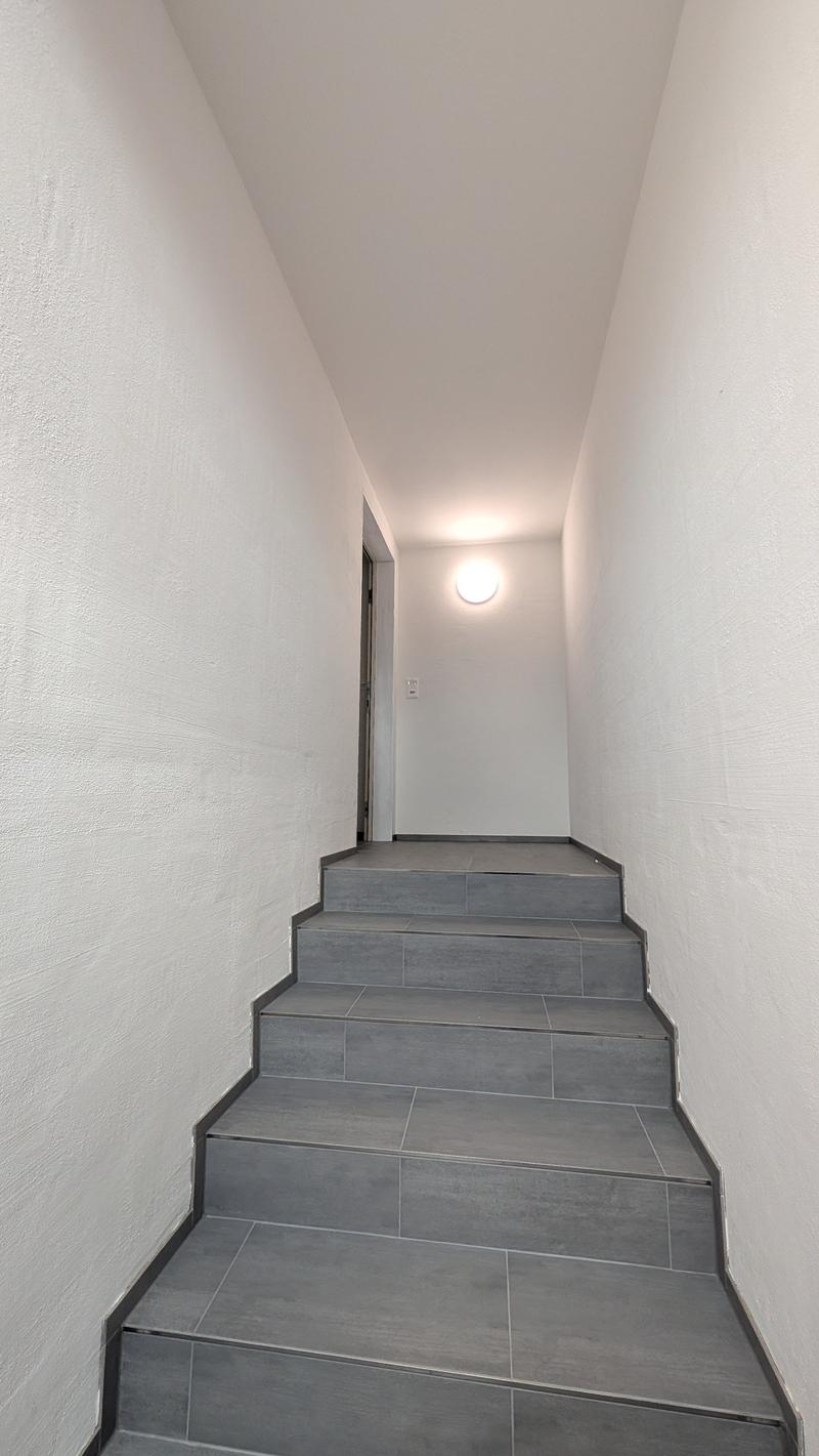 Staircase with gray tiles, white walls, ceiling light