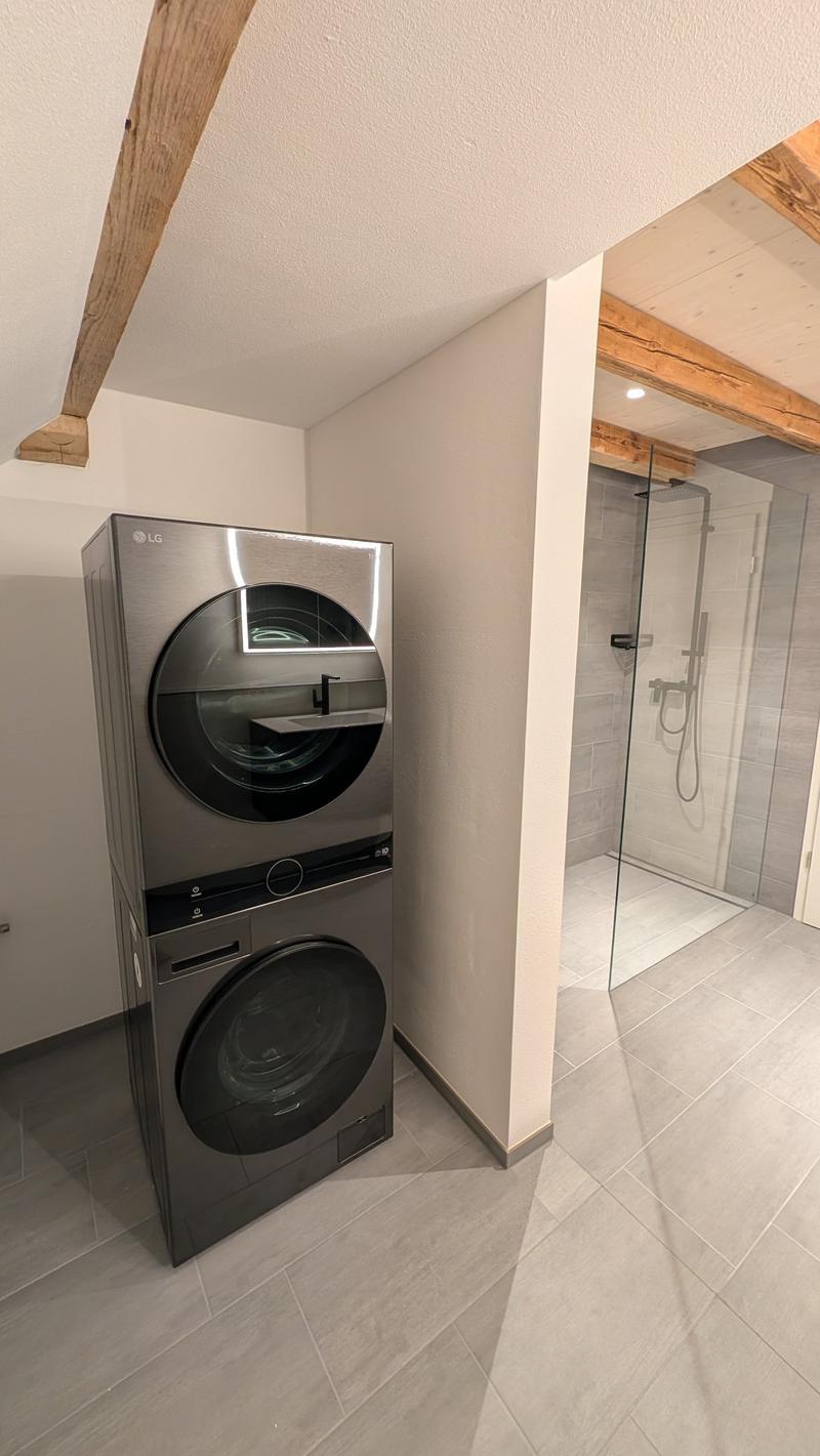 Laundry room with stacked LG washing machine and dryer, tiled floor, glass shower enclosure