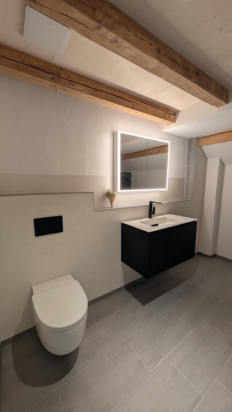 modern bathroom with white toilet, black vanity, white sink, mirror with lighting, wooden beams on ceiling