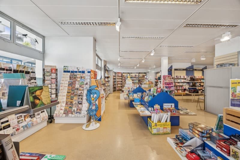 Large bookstore with shelves of books, toys, and other merchandise. Colorful displays and decorations, including a large cartoon character figure. The store appears well-lit and organized.