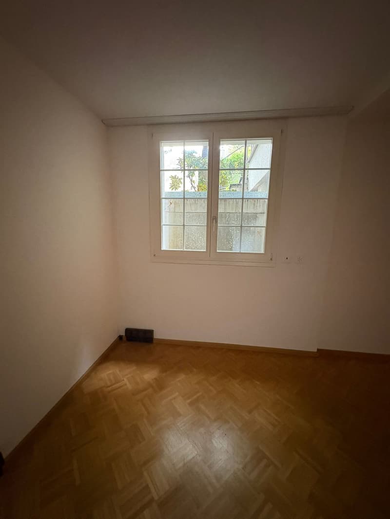 an empty room with wooden floor, a white wall, a window with a white frame, and power outlets