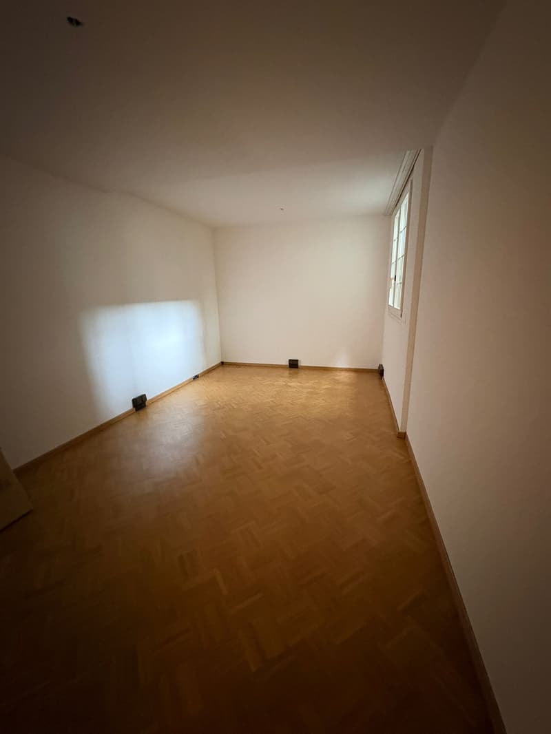 an empty room with wooden floor, white walls, and a window