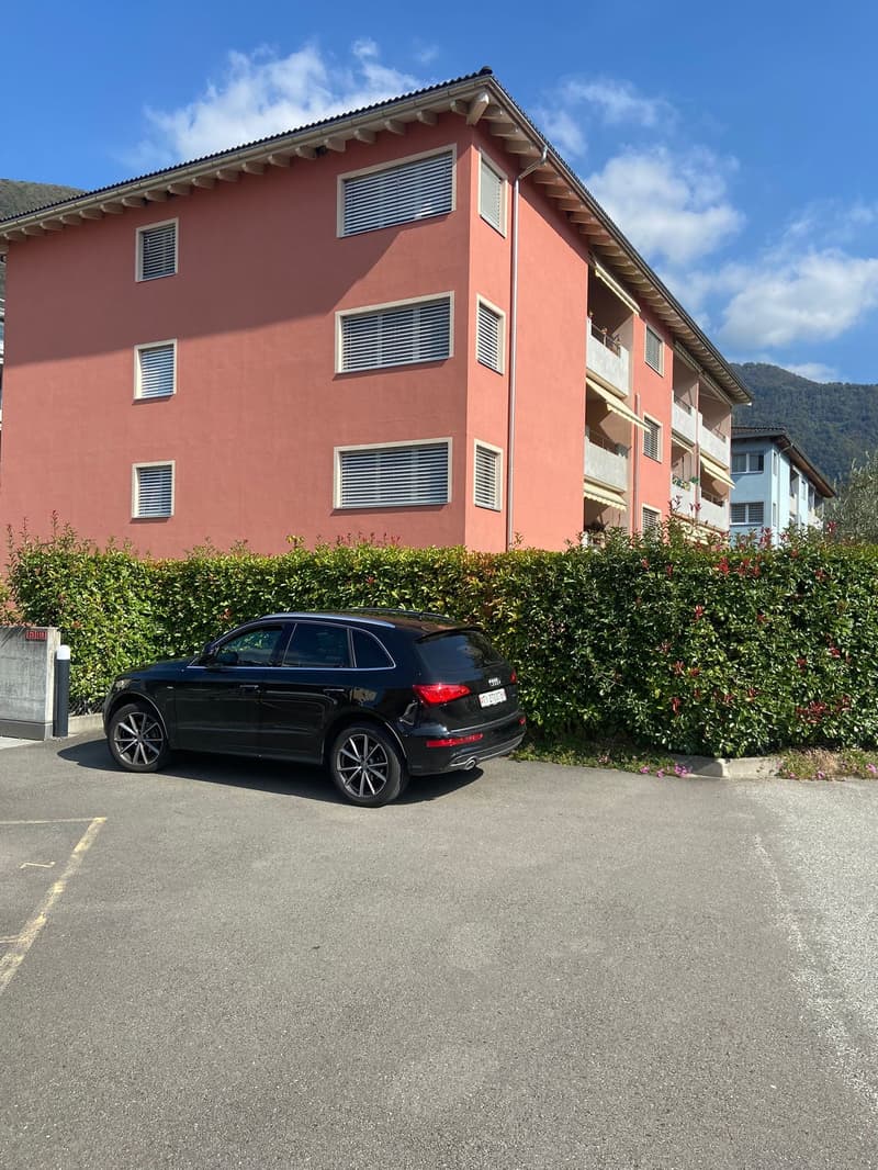Apartmens with multiple windows, a modern design with pink walls, a black SUV parked in front, bushes surrounding the property