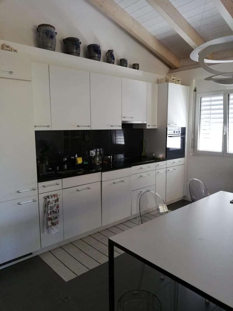 modern kitchen, white cabinetry, black countertops, built-in oven and stove, island with seating, large window with blinds, ceiling with wooden beams