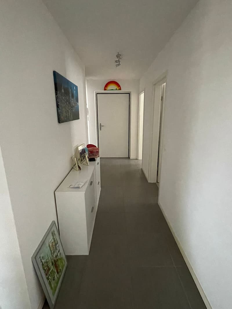 empty room, white walls, tiled floor, a white cabinet with pictures, a painting on the floor