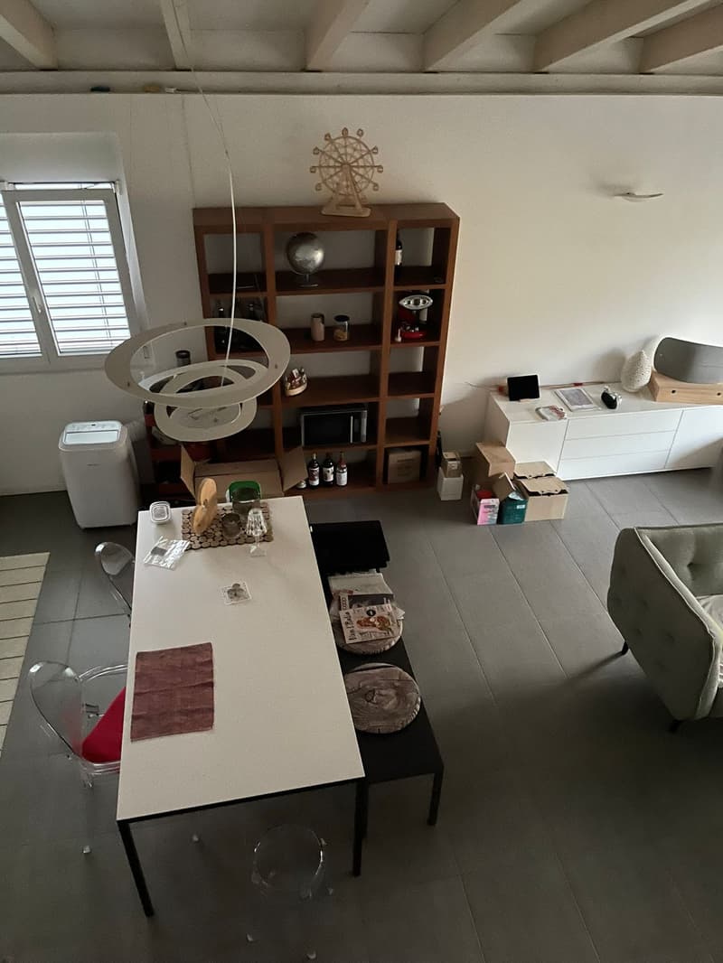 Open-plan living space, dining table, couch, large window, wooden shelf, storage boxes, open kitchen