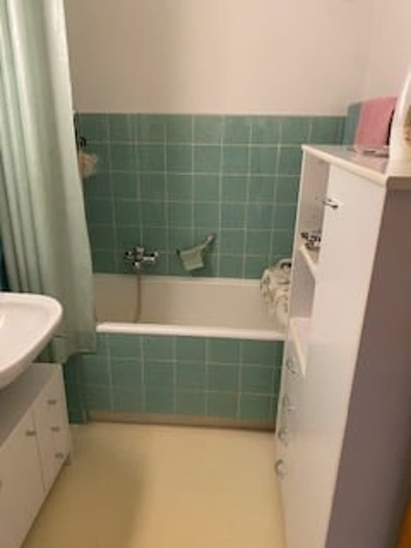 Bathroom with green tiles, bathtub, sink, shower curtain, and cabinets.