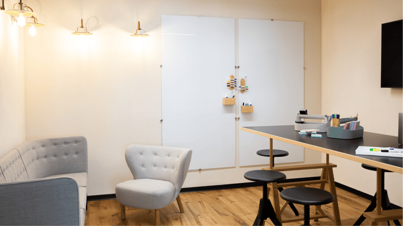office room with a couch, a chair, a desk, a board, a TV and a cabinet with a storage box