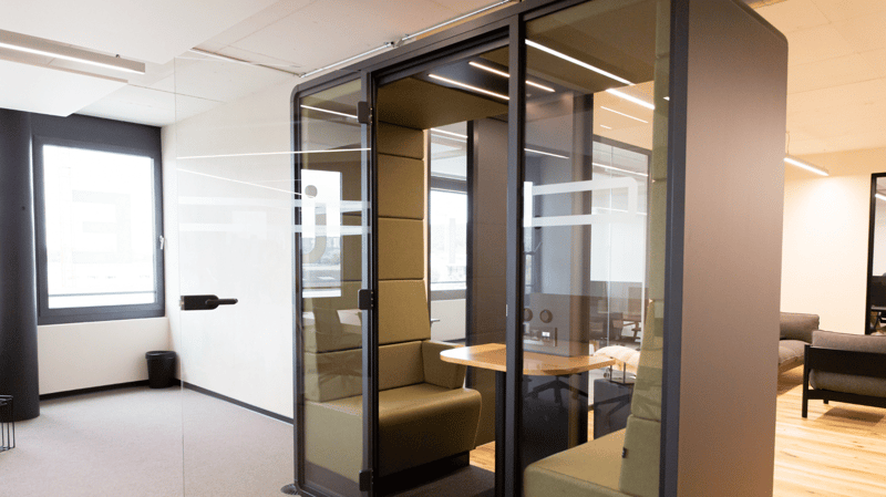 office with glass walls, beige upholstered chairs, wooden desk, black trash can, large window