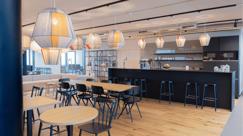 modern interior with wooden flooring, pendant lamps, kitchen area, bar counter, dining tables, chairs, white couch, shelves, open ceiling ducts
