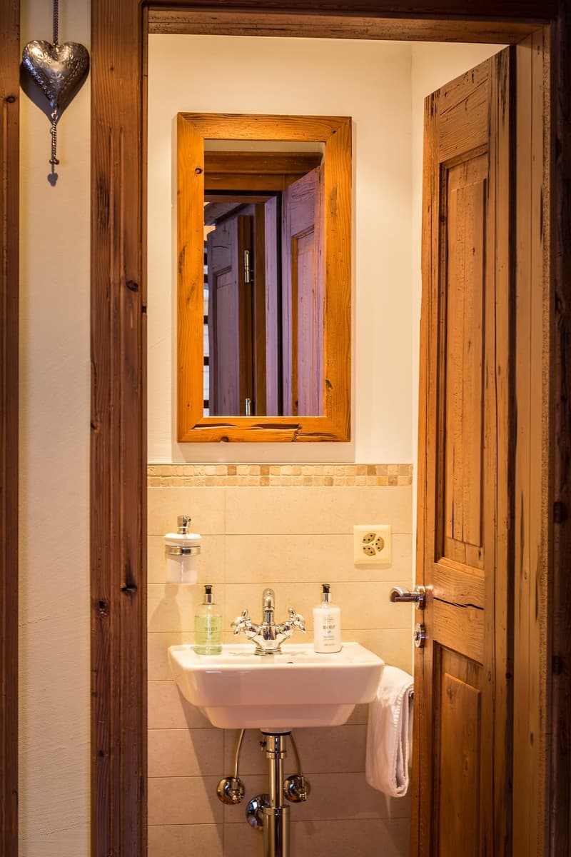 white sink, mirror, wooden door, toilet paper holder, soap dispensers, towels, soap and shampoo bottles