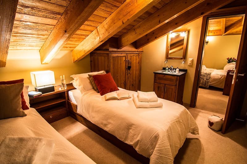 two beds, wooden wardrobe, wooden cabinet, wooden desk with lamp, books, towels, open mirror, wooden flooring