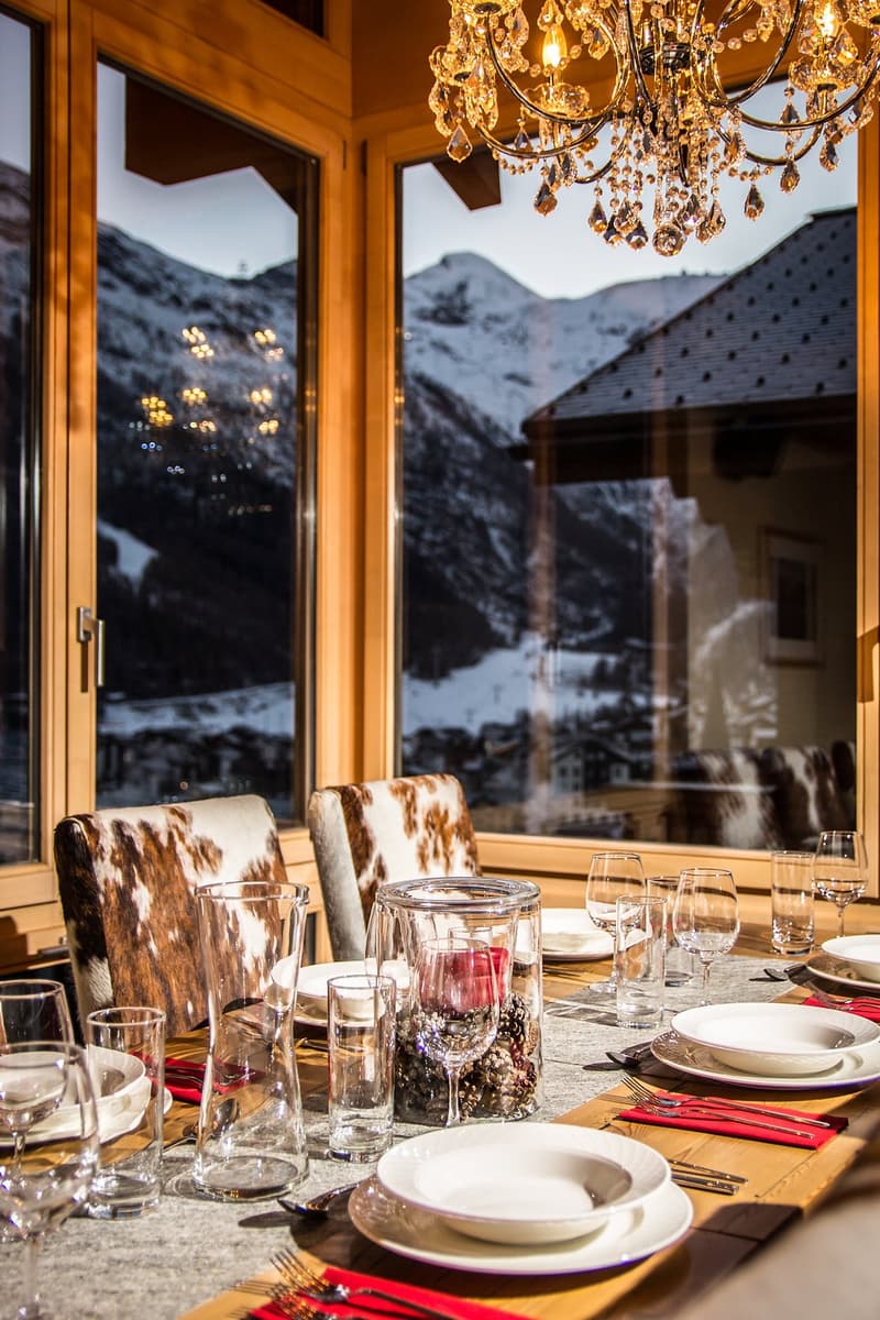 Set dining table with silverware, wine glasses, plates, cutlery, napkins, mountain view in the background, chandelier, two chairs with cowhide backs