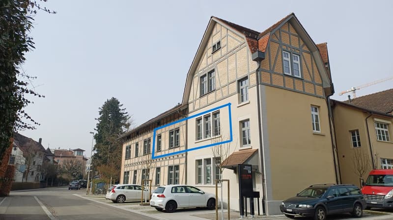 3 story house, beige brick, blue window frames, 3 windows on the second floor, 3 windows on the third floor, 3 windows on the ground floor, 2 cars parked in front