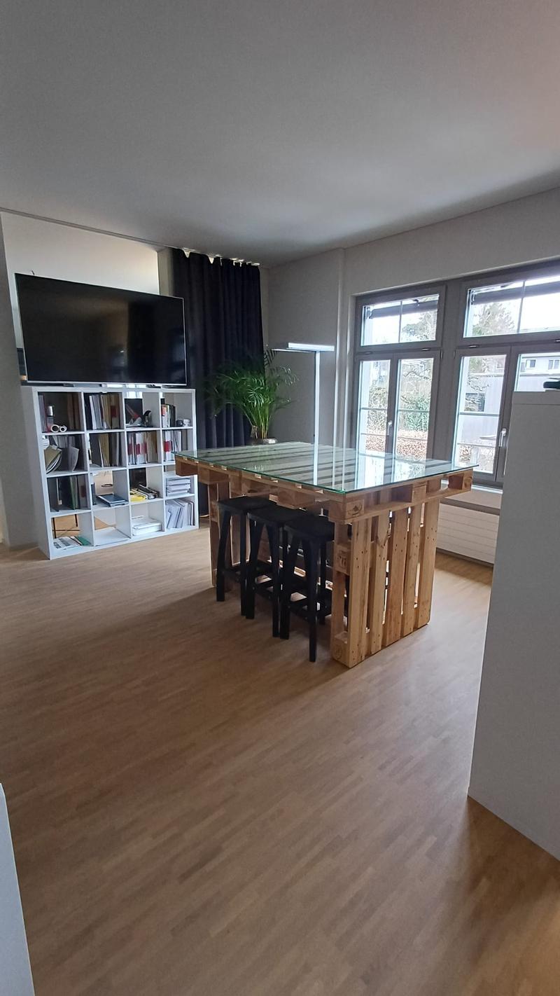 Living room with wooden floor, large glass table, TV, bookshelf, and windows