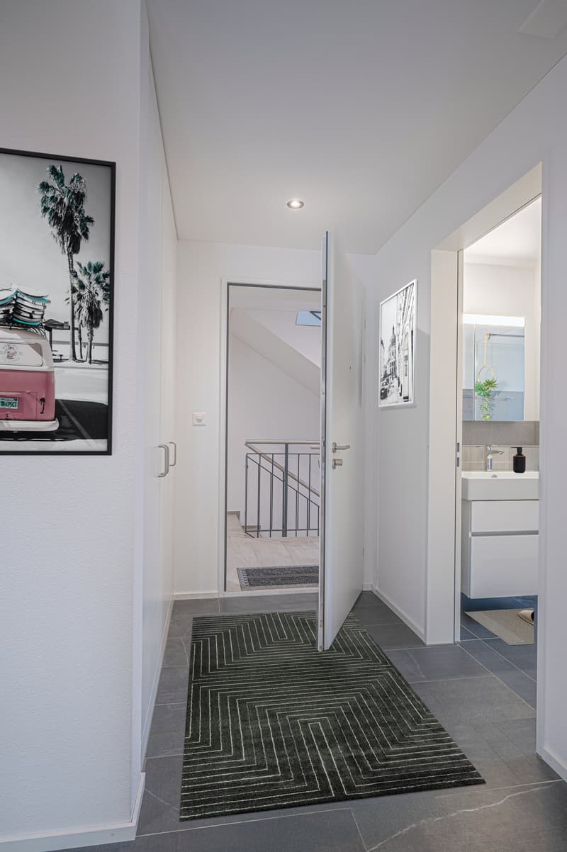 Entrance hall with open door, carpet, white walls, picture frame, mirror, sink, faucet, cabinet, staircase, and a glimpse of a bathroom