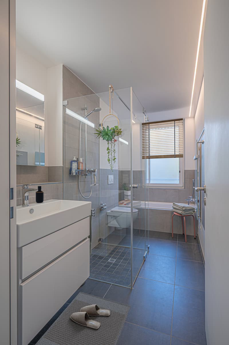 modern bathroom with glass shower, white sink, white tiles, mirror, toilet, bathtub, towel rack