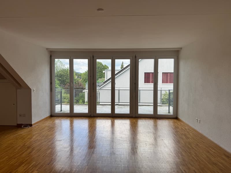 Spacious living room with large windows, hardwood floors, and access to a balcony or terrace overlooking the surrounding greenery.