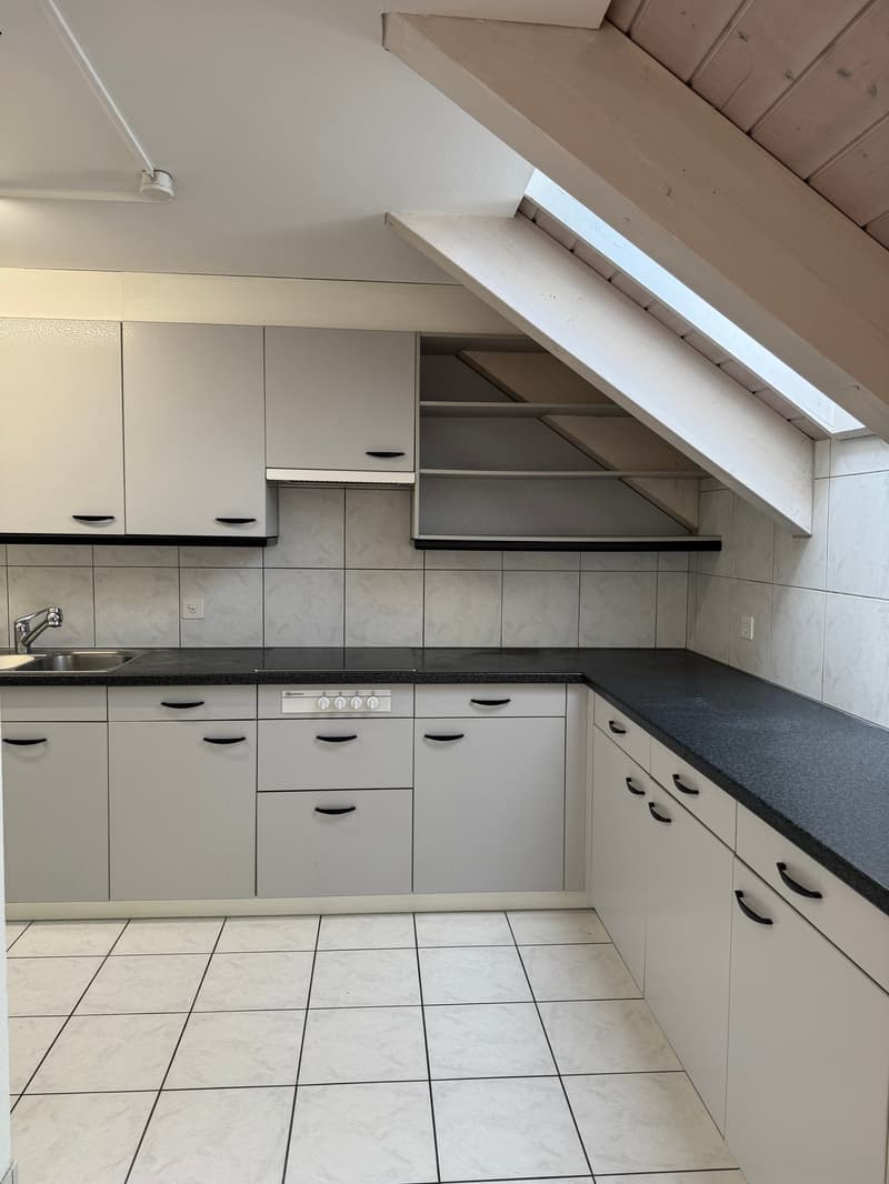 Attic kitchen with slanted ceiling, white cabinets, black countertops, tile flooring, and a dishwasher
