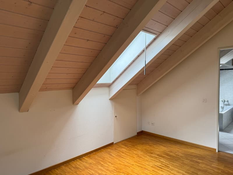 Attic or loft space with wooden beamed ceiling, white walls, and hardwood flooring. The room has a slanted ceiling with a skylight window providing natural light.