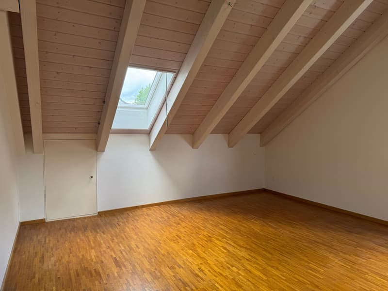 Attic space with wooden ceiling beams, hardwood flooring, and a skylight window providing natural light.