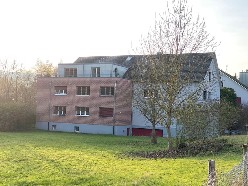 Multi-story building with brick facade, solar panels, and garage; surrounded by grass and trees