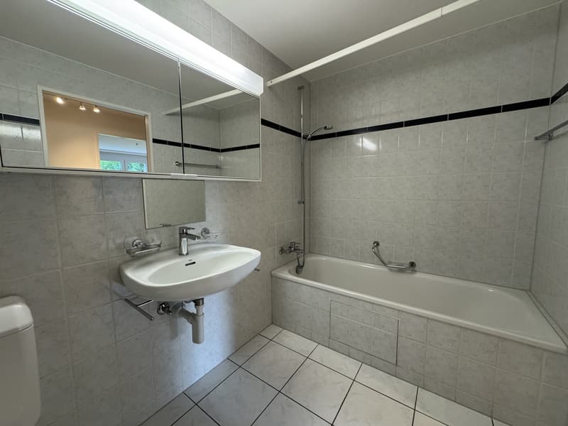 Bathroom with white tiled floor, bathtub, sink with mirror, toilet