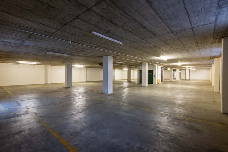 Large underground parking garage with concrete floors, columns, and overhead lighting. The space appears to be empty and unoccupied.