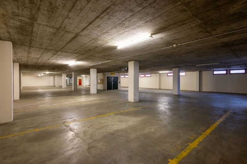 underground parking lot with concrete floors, yellow parking lines, several columns, some lights mounted on the ceiling