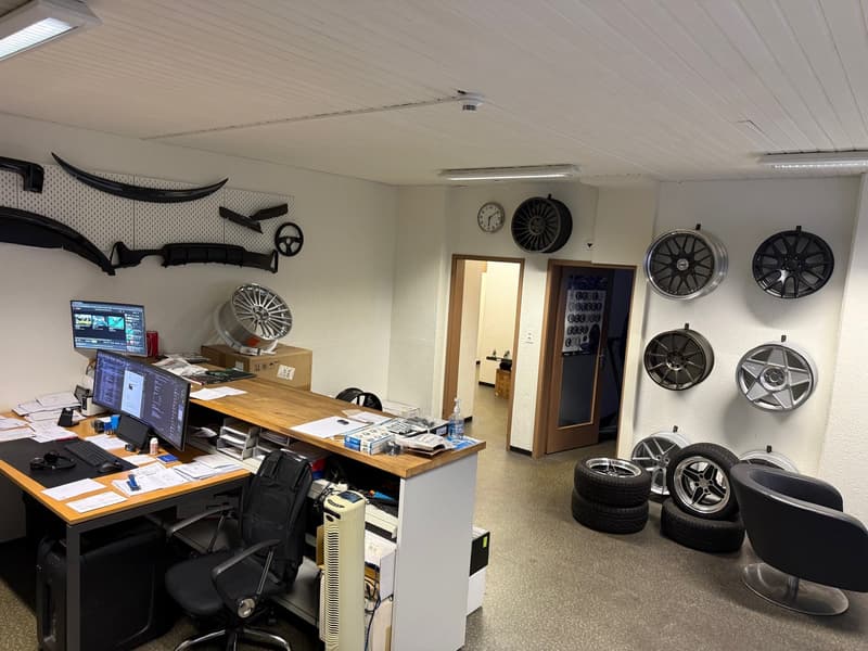 An office with a desk, chairs, computer monitors, a clock, tires, and wheels displayed on the walls.