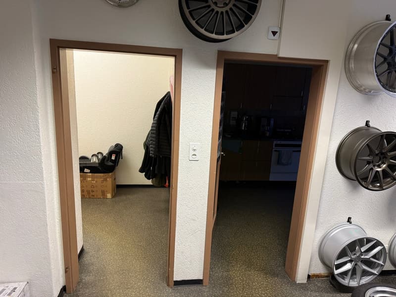 Corridor with open doors leading to adjacent rooms, coat rack with clothes, wheel rims mounted on wall, white ceiling, carpeted floor.