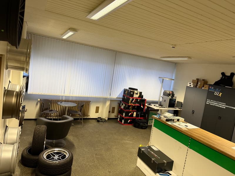 A room with multiple chairs and tables, stacks of boxes, storage cabinets, and a radiator. Tires and wheels are arranged on the floor.